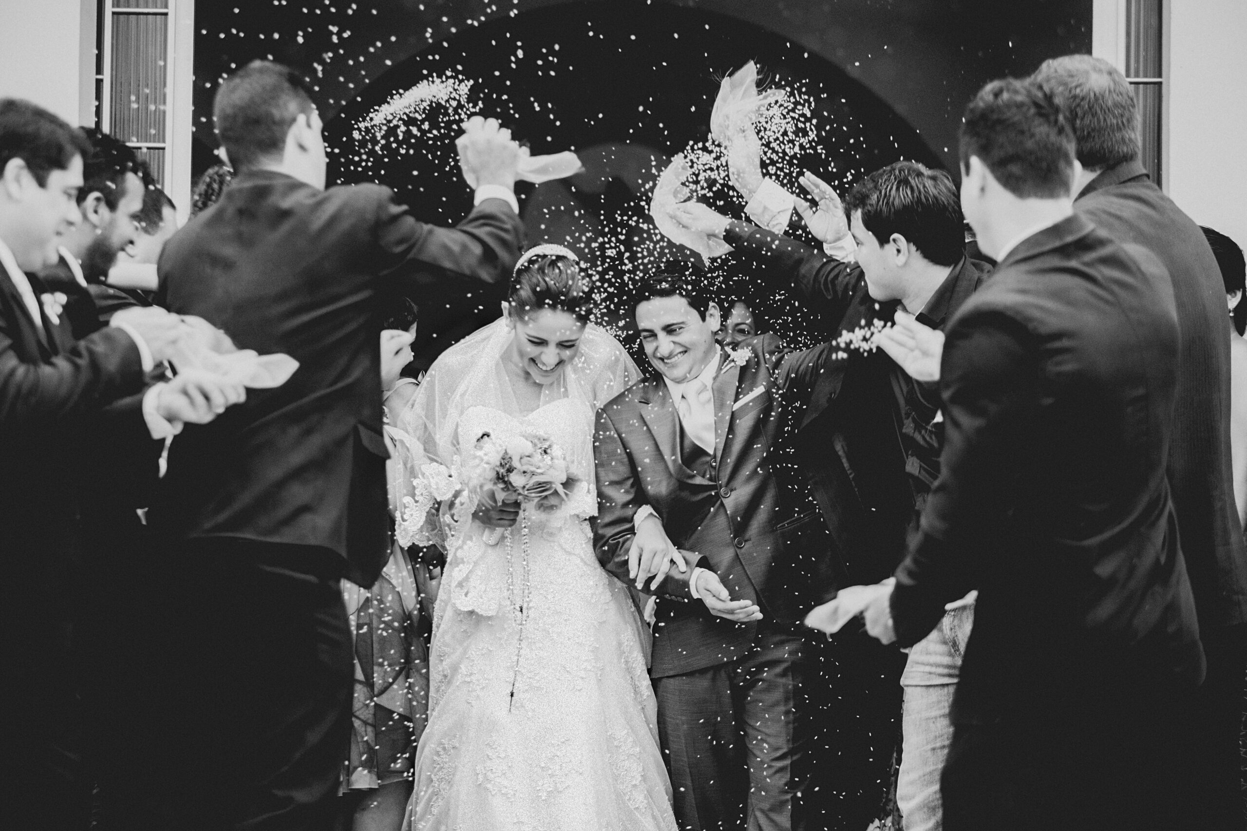 Newlyweds laughing as guests shower them with confetti, in black and white