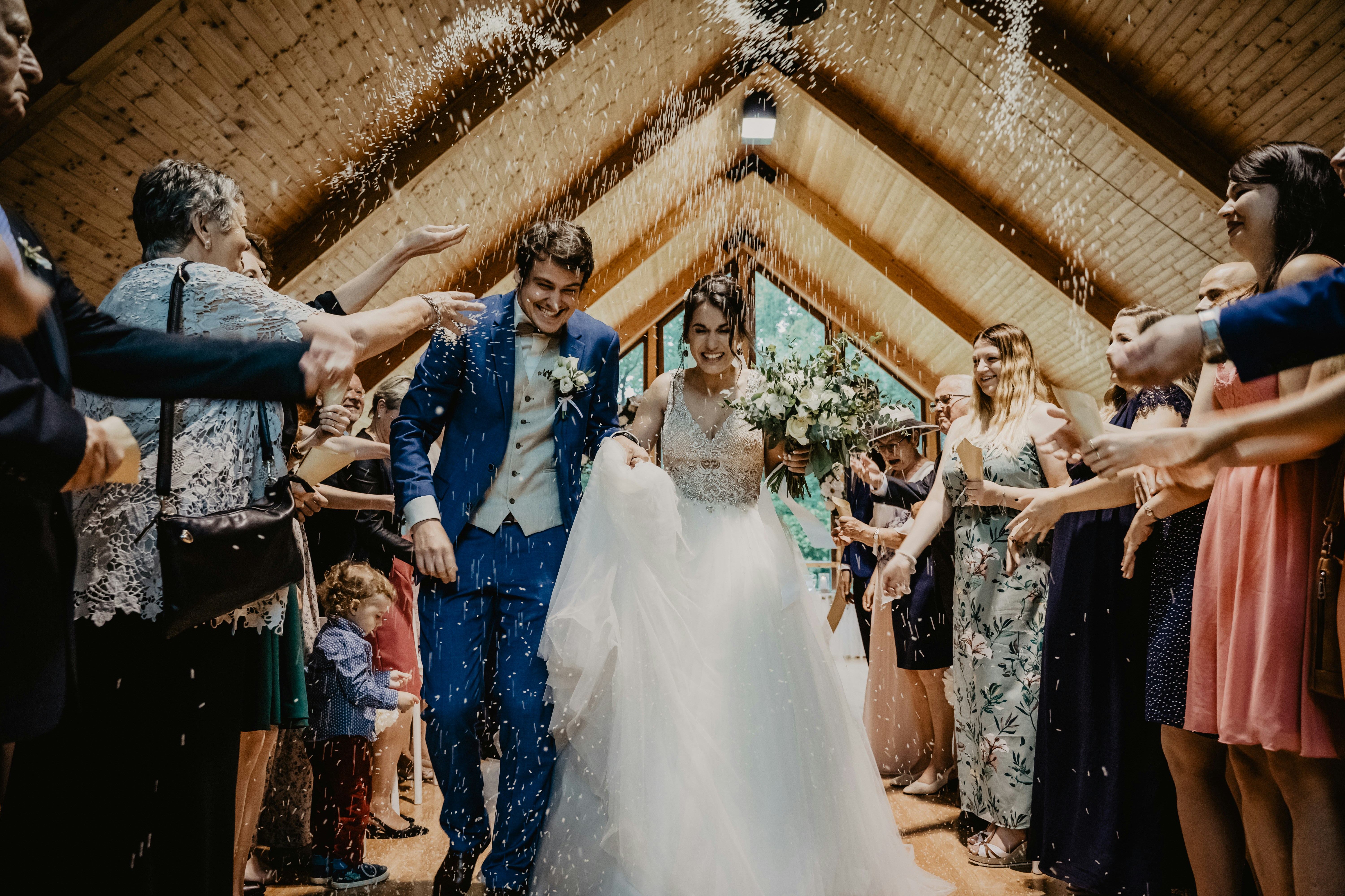 Bride and groom walking through a confetti toss beneath a timber-beamed ceiling